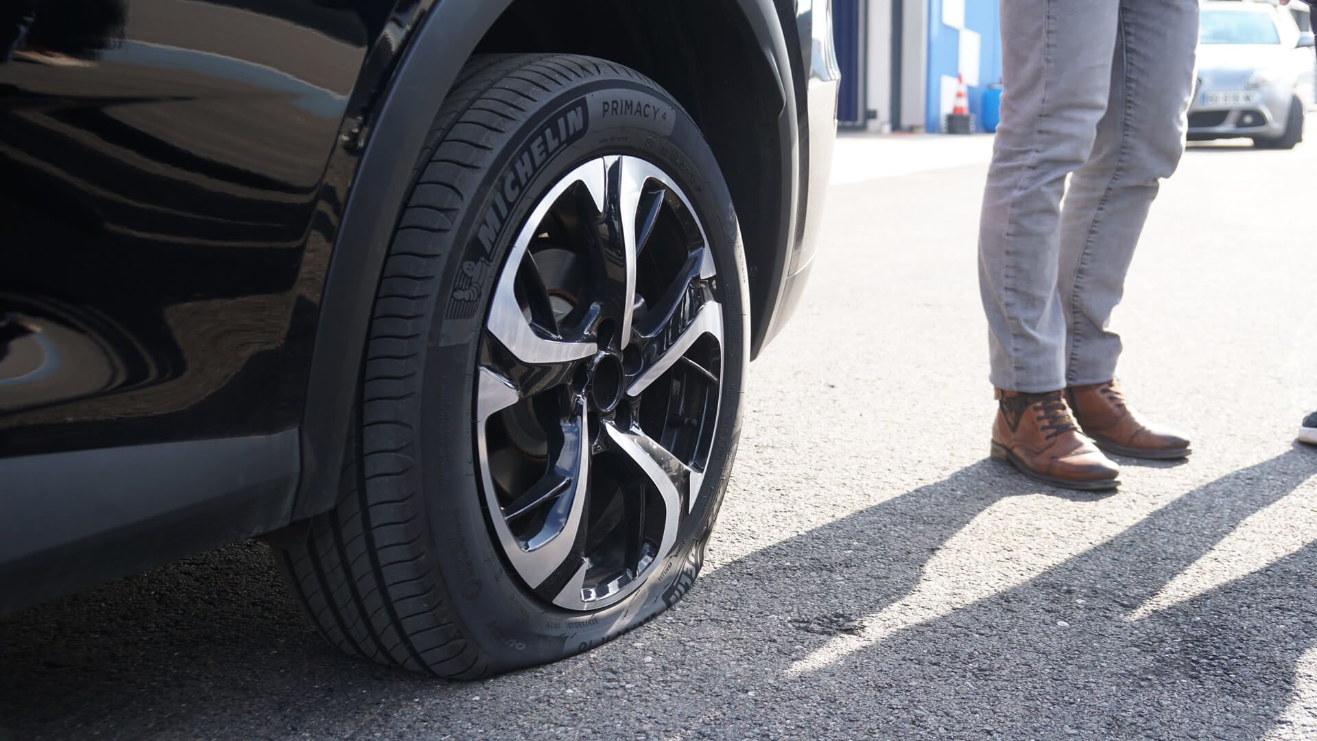 Close-up of a car tire punctured and deflated after contact with the SHARK SPIKE device, with two people standing nearby.