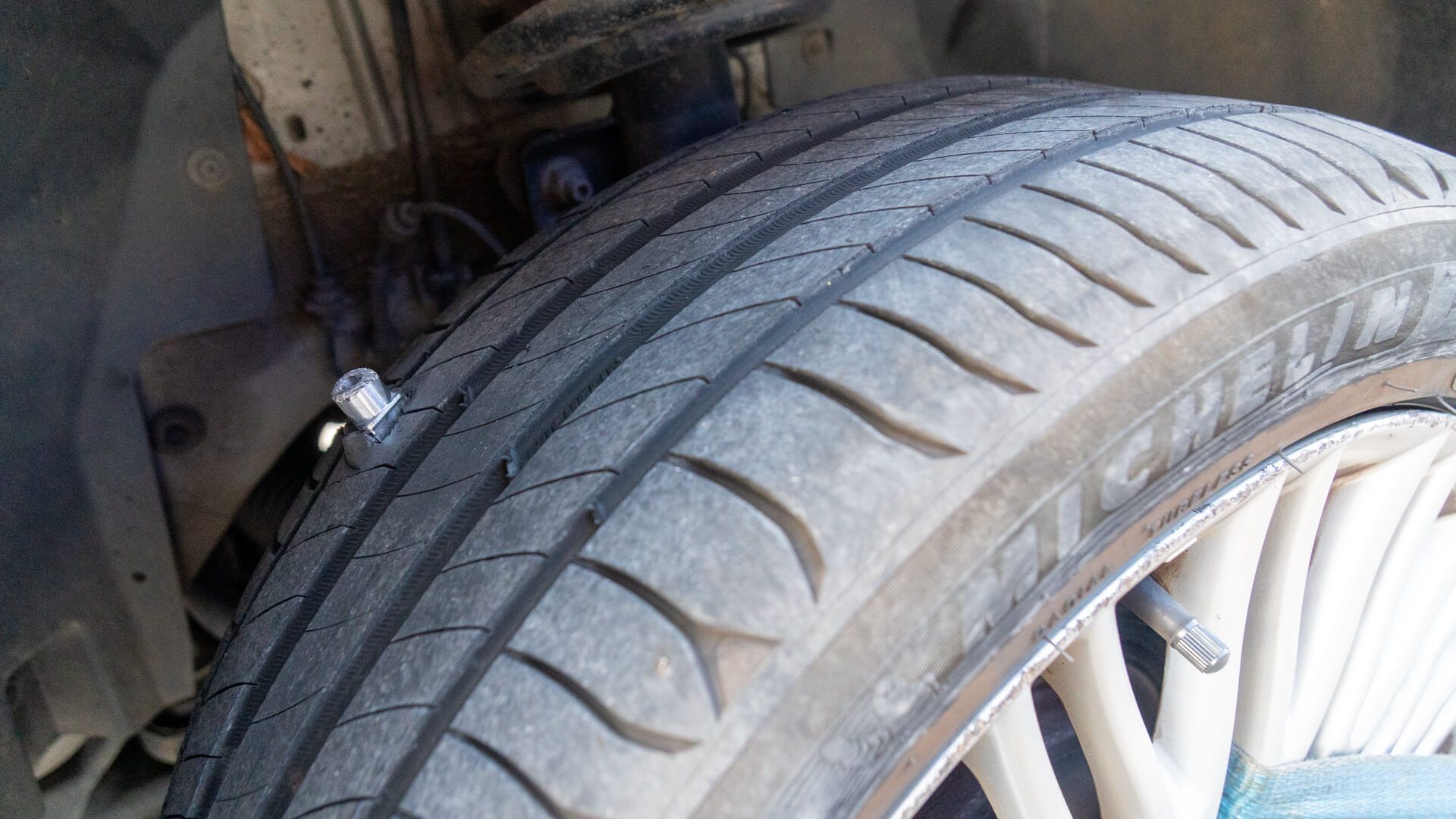 Close-up of a car tire with a visible spike lodged in the rubber, showing the effectiveness of the SHARK SPIKE device.