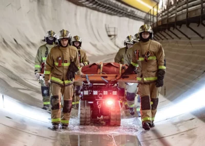 Firefighters escorting a rescue stretcher transported by Colossus robot inside a tunnel.